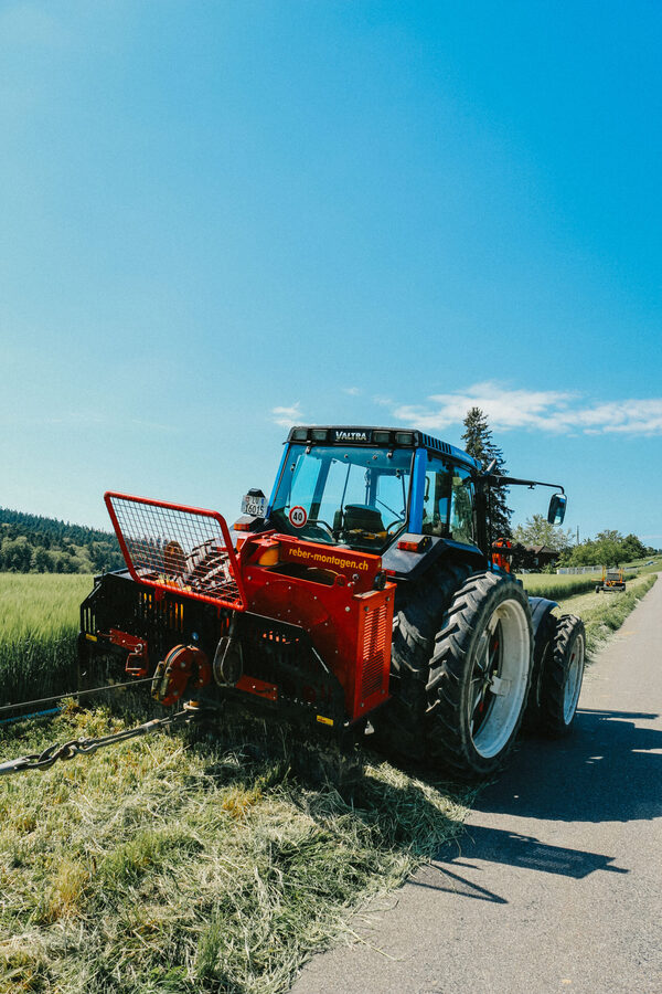 Ein roter Traktor der Firma Zemp Leitungsbau hält am Strassenrand neben einer Wiese