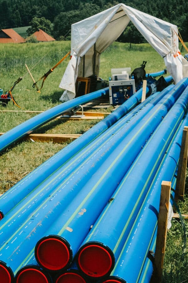 Blaue Leitungsröhren stehen bereit auf einer Wiese für den Einbau im Graben