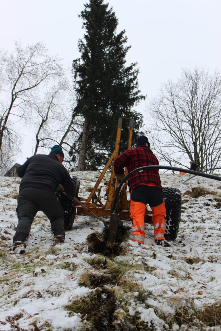 Zwei Mitarbeiter der Firma Grabenlos AG arbeiten engagiert im Hang daran, eine Wasserleitung zu verlegen mit der Pflügmaschine. Die Hanglage stellt sie vor eine anspruchsvolle Aufgabe, doch mit Fachkenntnis meistern sie die Herausforderung souverän.