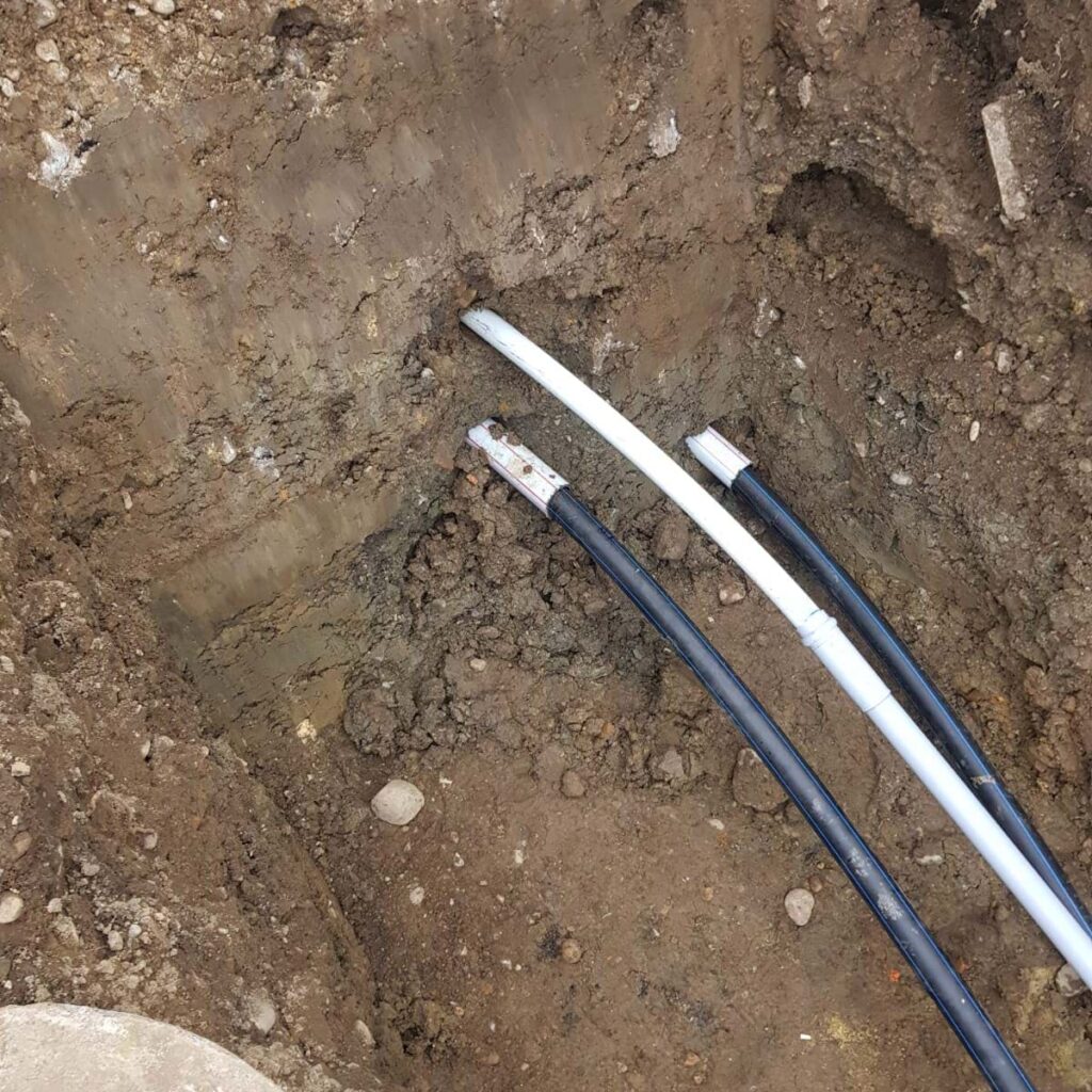 Im Graben befinden sich drei Rohre, diese wurden bereits verlegt und ragen noch aus dem Boden heraus, bis die nächsten Arbeitsschritte durchgeführt wird.