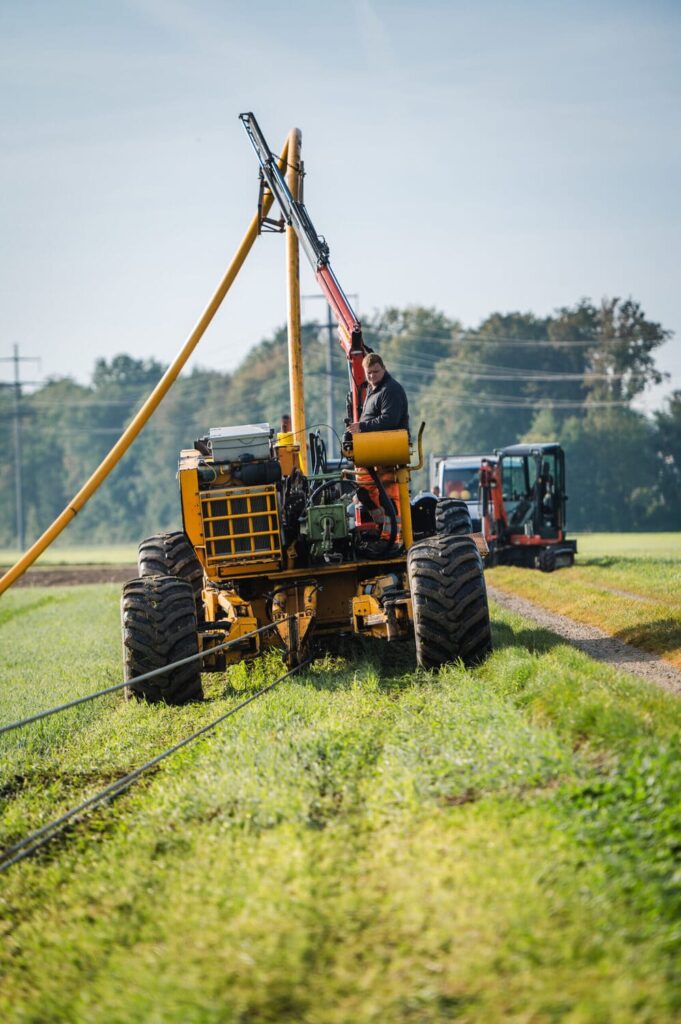 Der Mitarbeiter ist mit der Pflugmaschine auf dem Feld unterwegs, um Rohrkanäle unter der Erde zu verlegen. Die Maschine lockert und bearbeitet die Erde, damit die Rohrleitungen präzise installiert werden können.