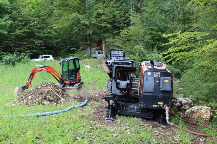 Am Waldrand stehen ein Bagger und eine Bohrungsmaschine der Firma Grabenlos AG bereit. Beide Maschinen sind für die bevorstehenden Arbeiten zur Verlegung der Entwässerungsleitung vorbereitet und warten auf ihren Einsatz.