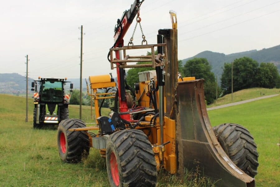 Auf einen Feld steht eine Einpflügmaschine zum verlegen von Kabel, Leitungen und Rohren. Im Hintergrund steht ein Traktor.