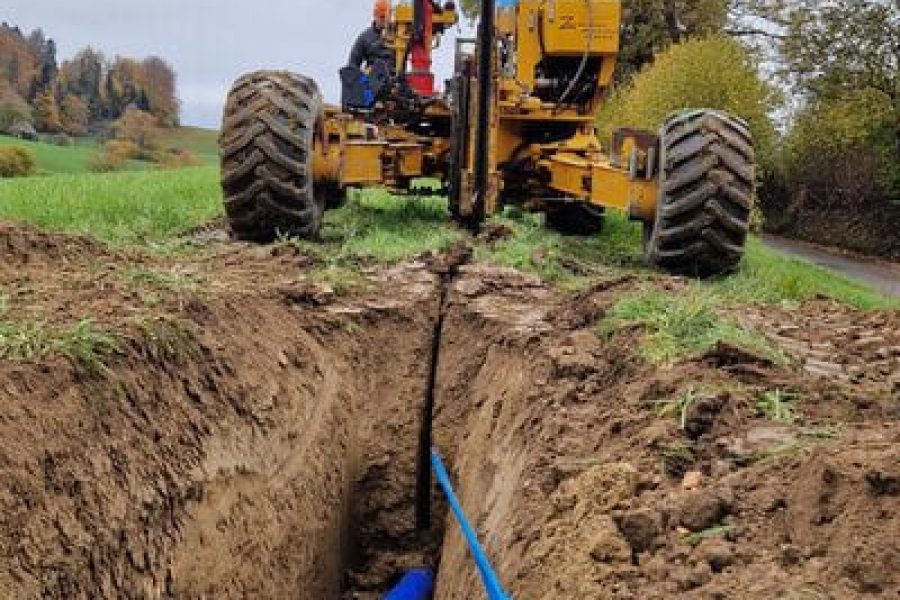 Eine Trinkwasserleitung findet ihren Weg in den Boden, während eine Pflügmaschine einen Graben zieht. Diese technische Meisterleistung ermöglicht es, die Leitung präzise und effizient zu verlegen.